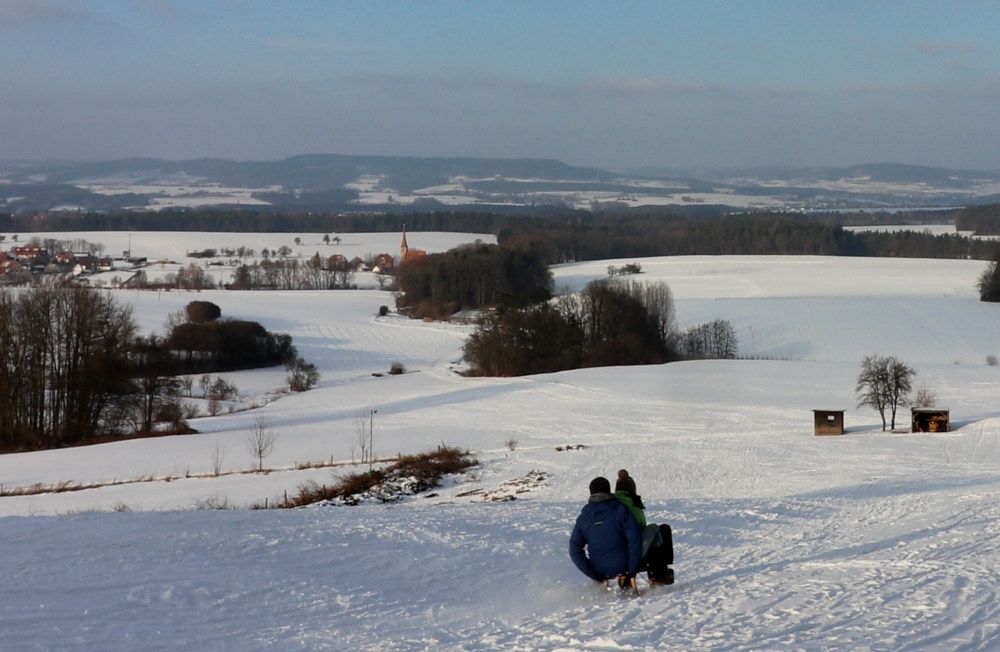 Der Tauchersreuther Rodelhang und im Hintergrund die Beerbacher Kirche, an der sich der Wanderparkplatz befindet